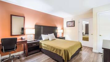 A hotel room with a bed, desk, chair, and a door.