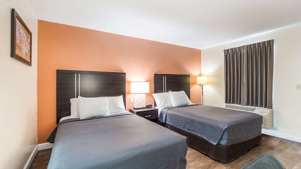 Une chambre d’hôtel avec deux lits, un bureau, une chaise, une lampe et une fenêtre avec des rideaux.