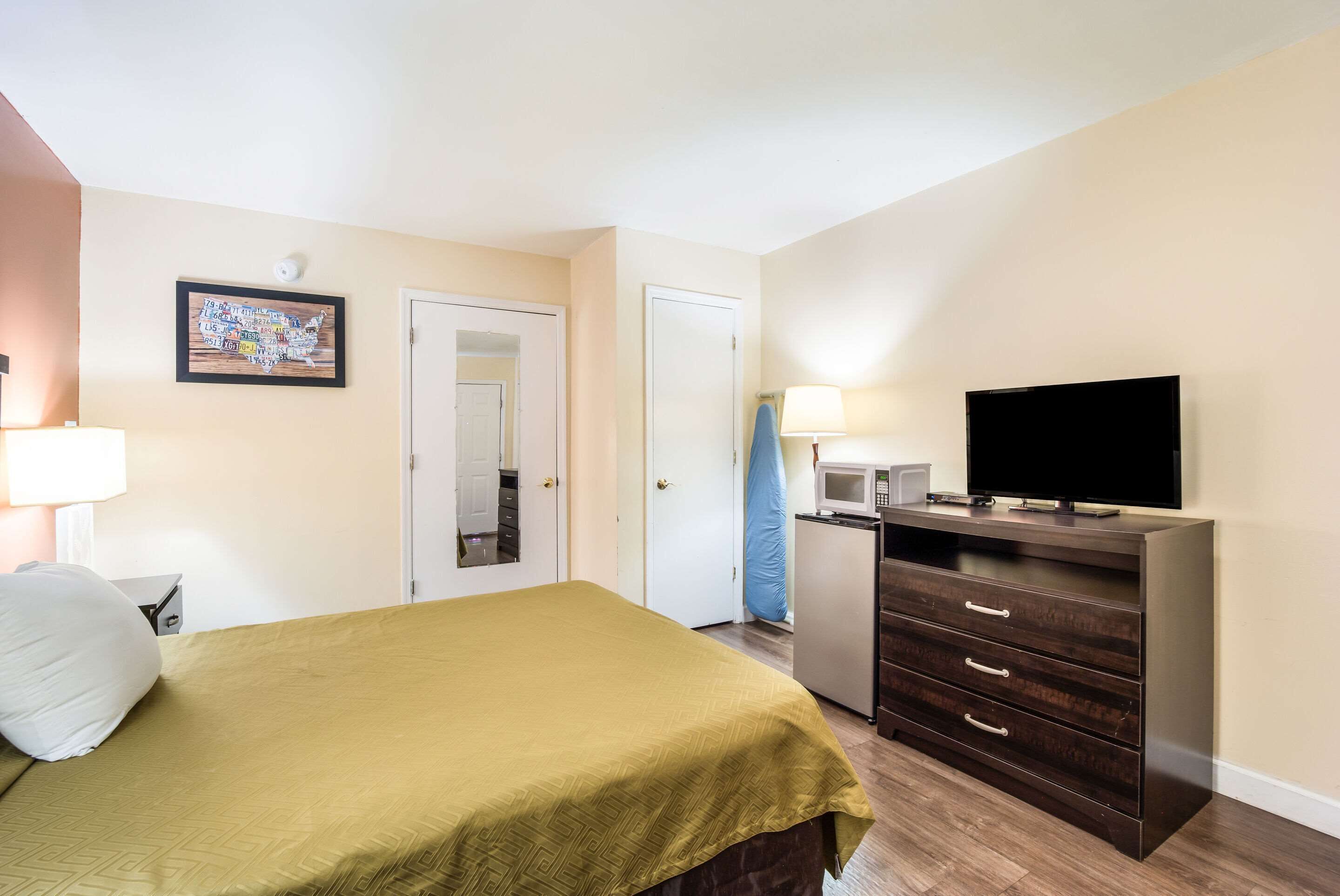 A hotel room with a bed, a dresser, a television, a microwave, and a door.