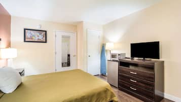A hotel room with a bed, a dresser, a television, a microwave, and a door.