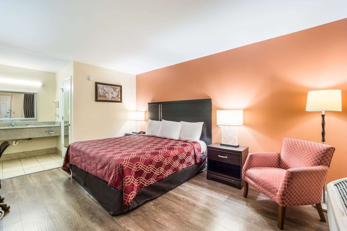 A hotel room with a bed, nightstands, a chair, a desk, and a mirror.