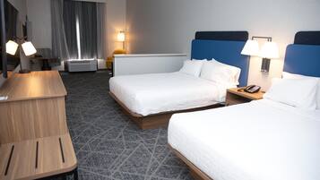 Quarto de hotel com duas camas, uma escrivaninha, uma cadeira, um abajur e um telefone na mesa de cabeceira.