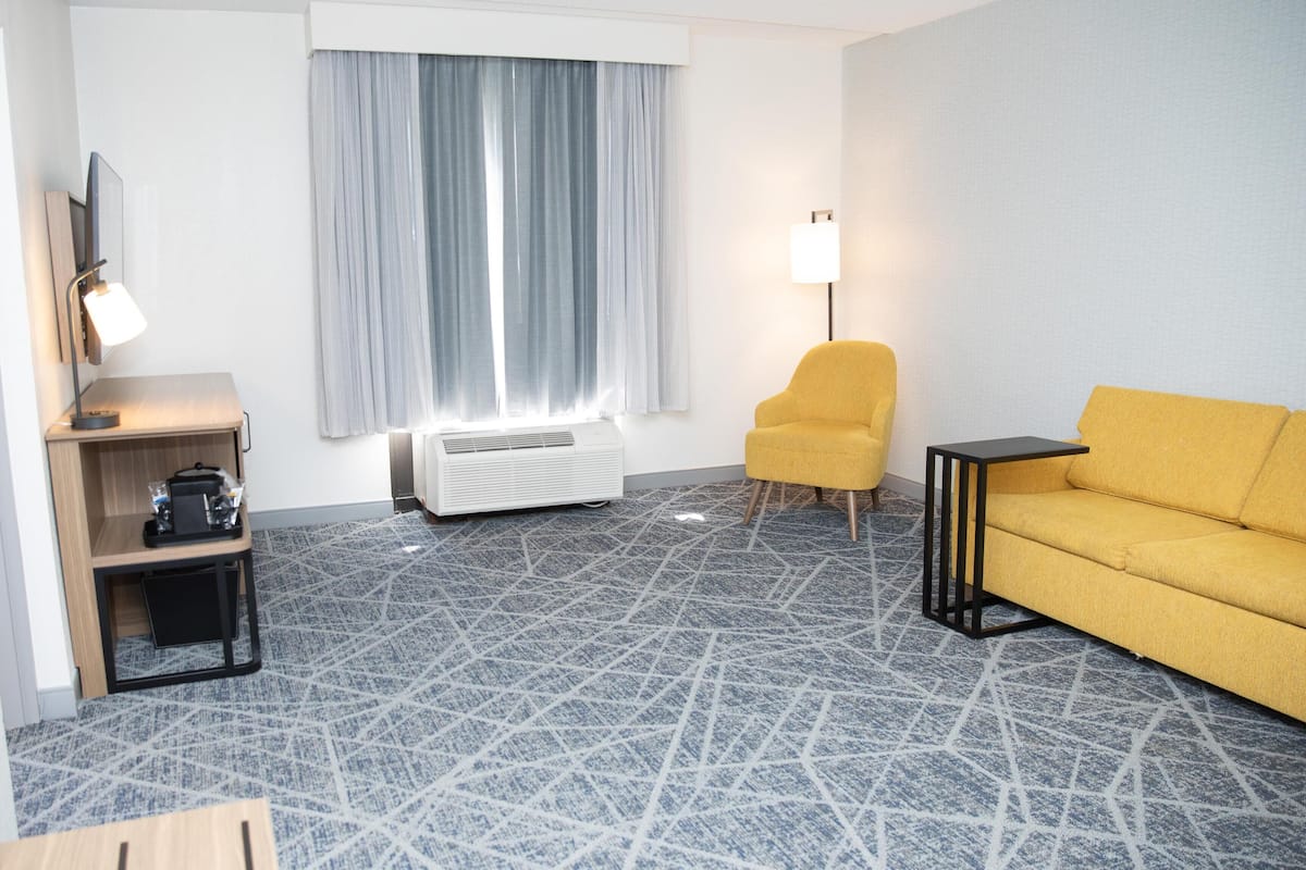 Ein Hotelzimmer mit einer Couch, einem Sessel, einer Lampe, einem Heizgerät und einem kleinen Tisch.