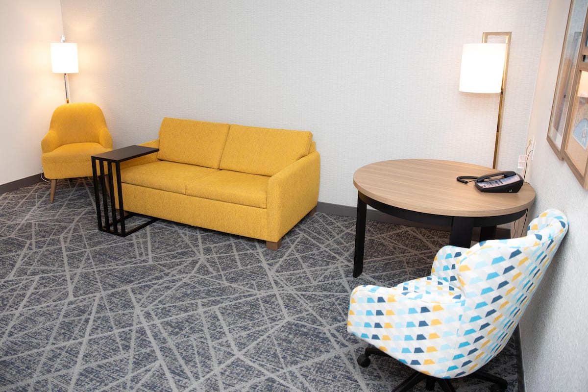 Ein Hotelzimmer mit einer Couch, einem kleinen Tisch, einem Sessel, einem runden Tisch und einer Lampe.