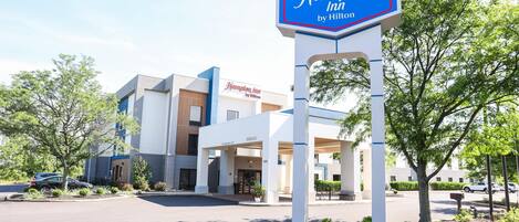 A Hampton Inn by Hilton hotel with a clear entrance, a signboard, and a parking lot.