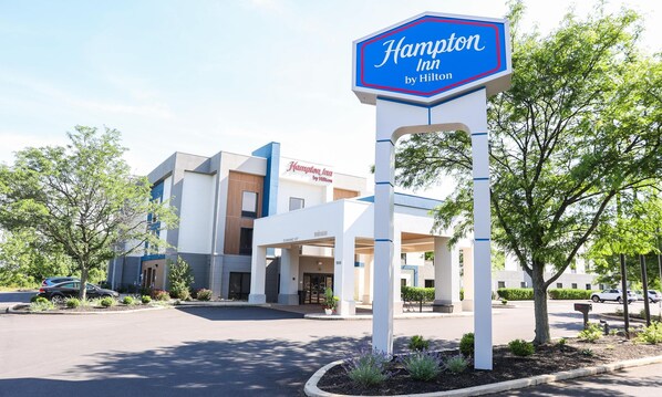 A Hampton Inn by Hilton hotel with a clear entrance, a signboard, and a parking lot.
