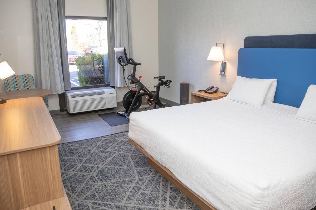 Ein Hotelzimmer mit Bett, Schreibtisch, Lampe, Telefon und Fahrrad.