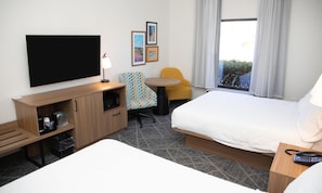 A hotel room with a bed, a desk with a TV, a chair, a small table, and a window with curtains. - Hampton Inn Shrewsbury (New Freedom)
