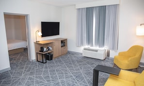 A hotel room with a bed, a desk with a flat-screen TV, a chair, a heater, and a window with curtains. - Hampton Inn Shrewsbury (New Freedom)