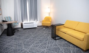 A hotel room with a sofa, a chair, a small table, an air conditioning unit, a lamp, and a patterned carpet. - Hampton Inn Shrewsbury (New Freedom)