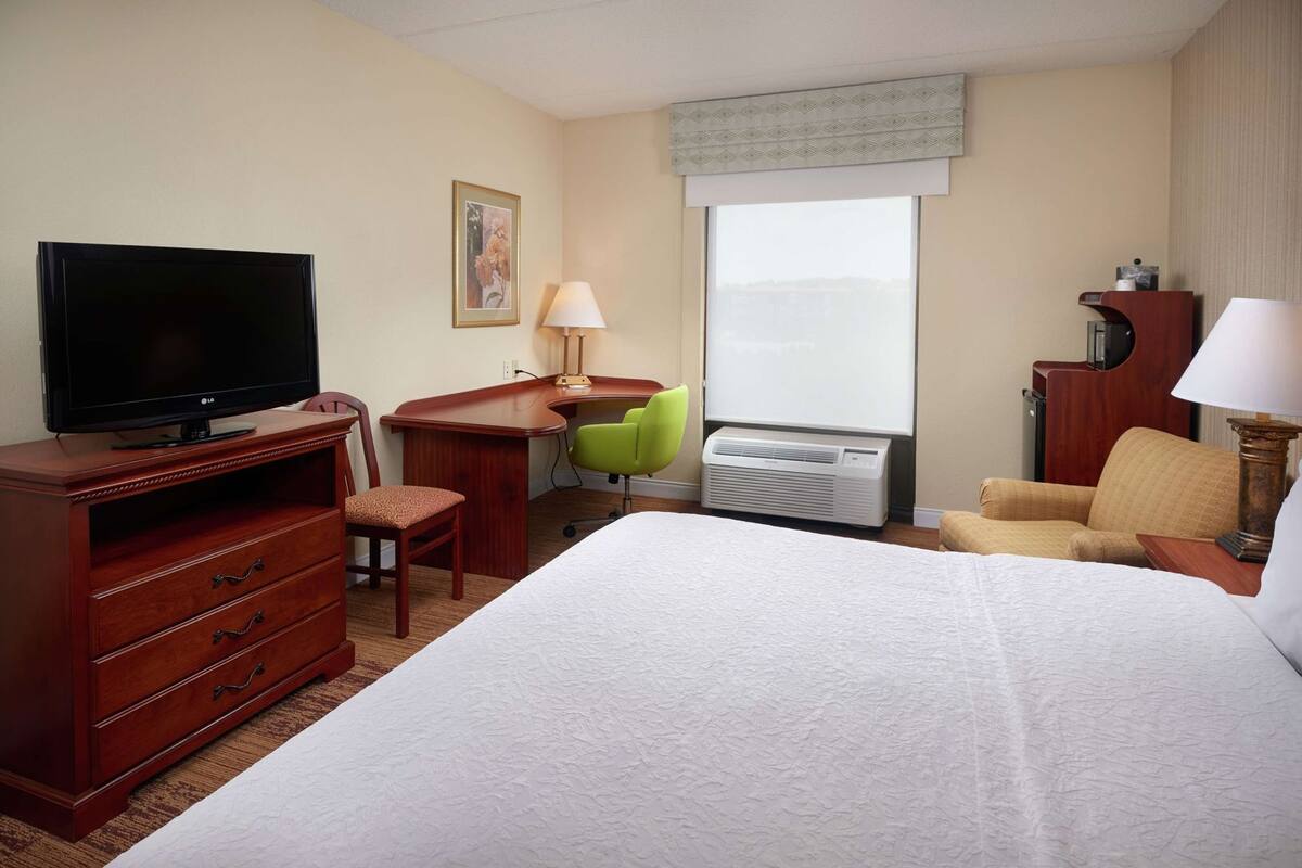 Ein Hotelzimmer mit Bett, Schreibtisch mit Fernseher, Stuhl, Klimaanlage und Fenster.