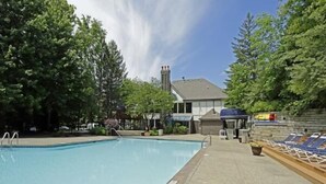 A swimming pool with lounge chairs, a covered seating area, and a building with a chimney in the background. - Oakwood River Oaks North (Rochester)