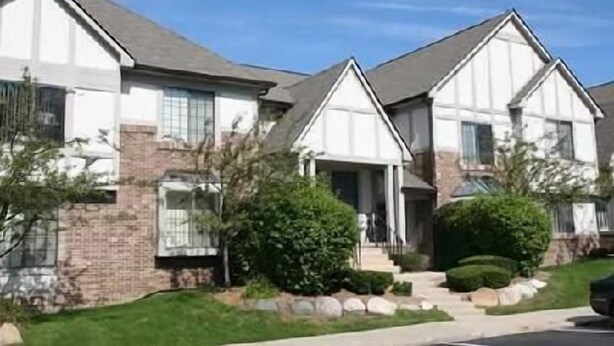 A row of two-story houses with brick and white siding, a well-maintained lawn, and a clear sky. - Oakwood River Oaks North (Rochester)