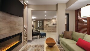 A modern living room with a flat-screen TV, a wooden coffee table, and a green sofa with red cushions. - Country Inn & Suites by Radisson, Bakersfield, CA (Bakersfield)