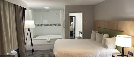 A hotel room with a large bed, bedside table, lamp, and a view of the bathroom.