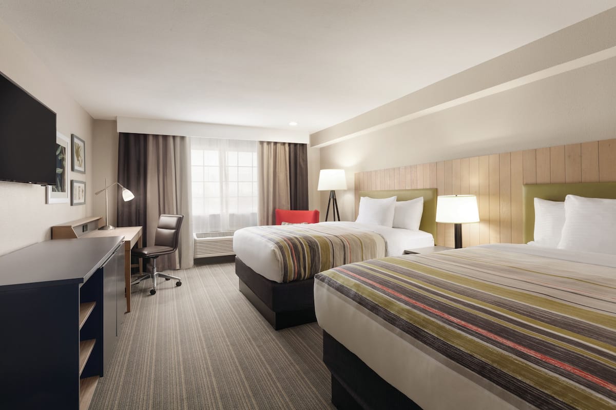 A hotel room with a large bed, a desk, a chair, and a TV.