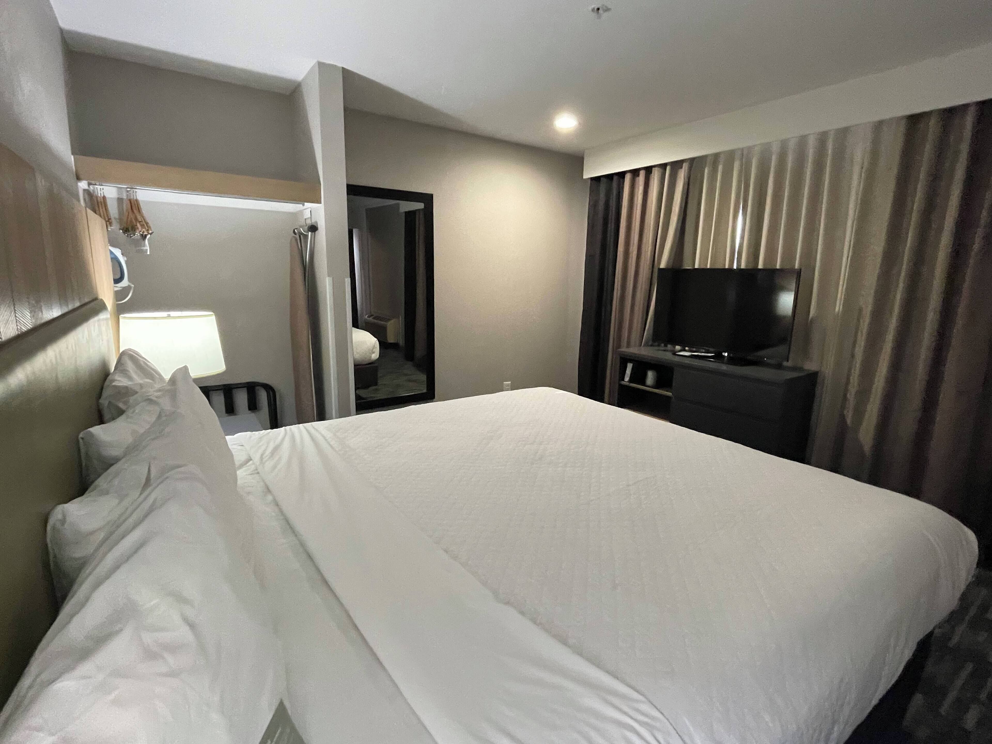 Habitación de hotel con una cama grande, un televisor sobre un mueble, un escritorio y un espejo.
