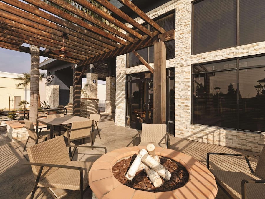 Un espacio al aire libre con mesas y sillas, un pozo de fuego y una estructura de pérgola.