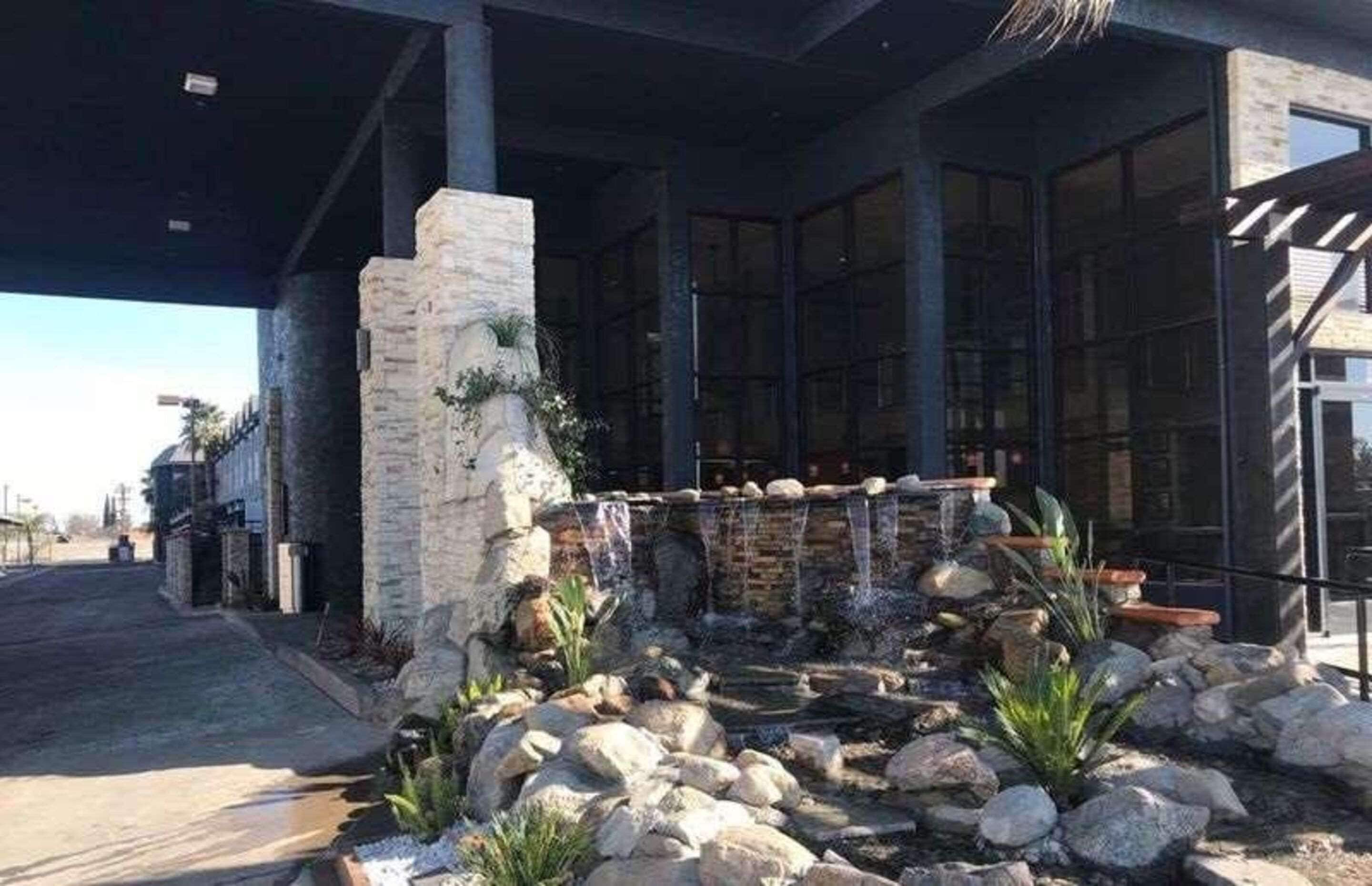 Un bâtiment doté d’une façade en pierre, d’une cascade décorative et d’un espace d’entrée pavé.