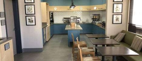 A compact kitchen with a central island, a dining area with a sofa and chairs, and framed artwork on the walls.