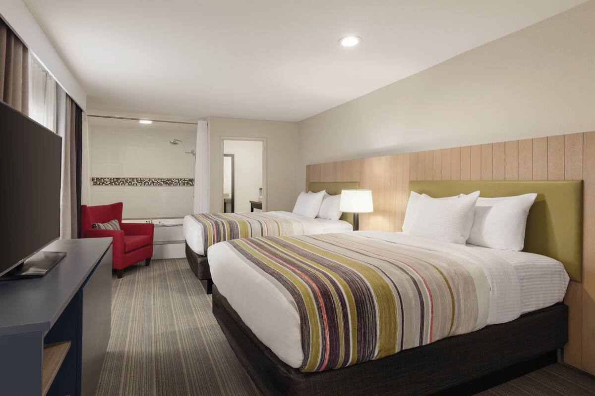 A hotel room with two beds, a desk, a red chair, and a TV.