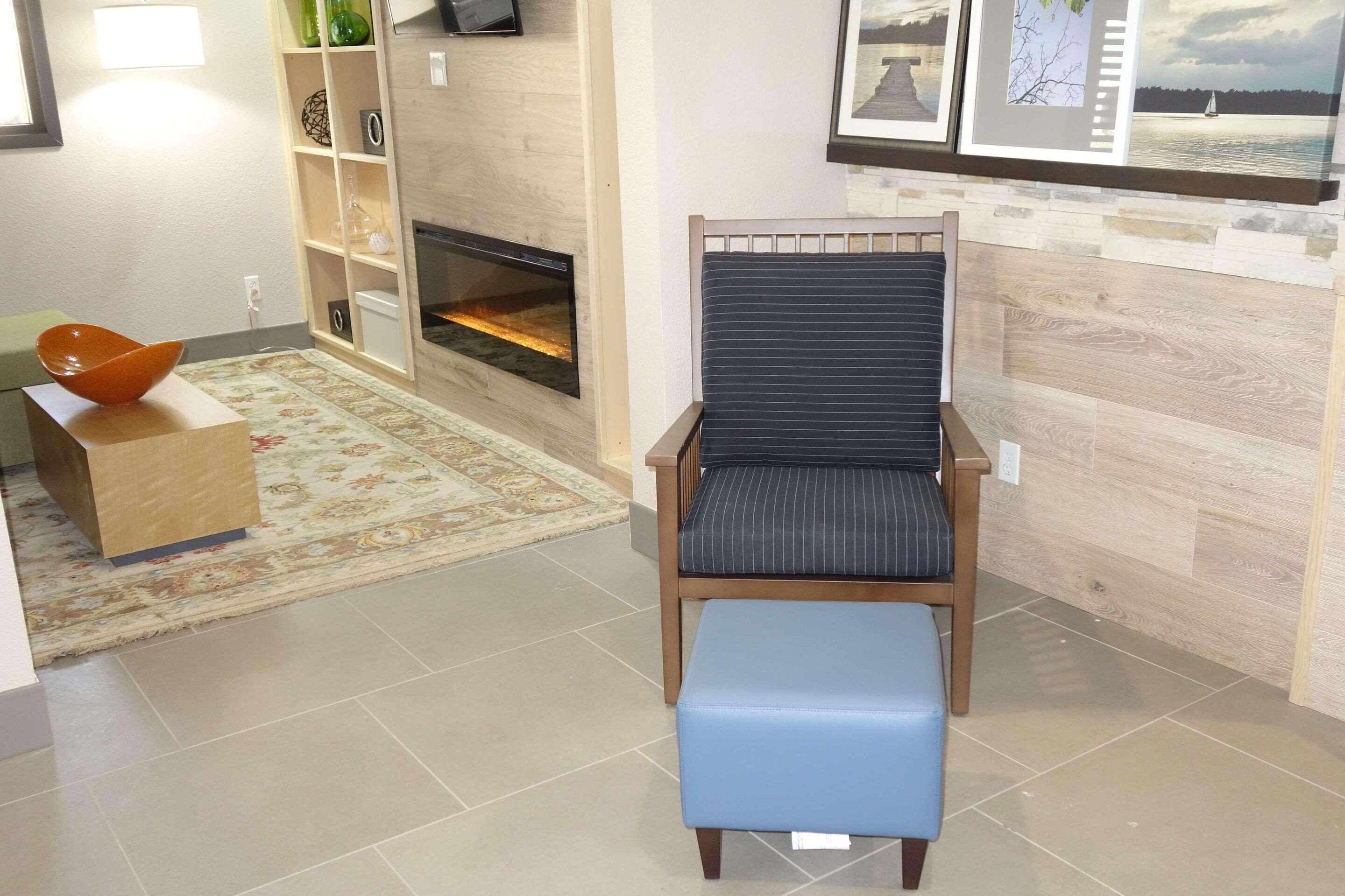Un salon avec une cheminée, un pouf bleu et une chaise en bois avec un coussin à rayures.