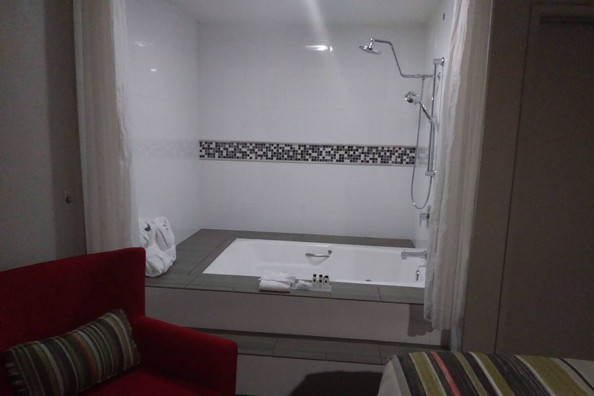A hotel bathroom with a bathtub, shower, and a red chair.