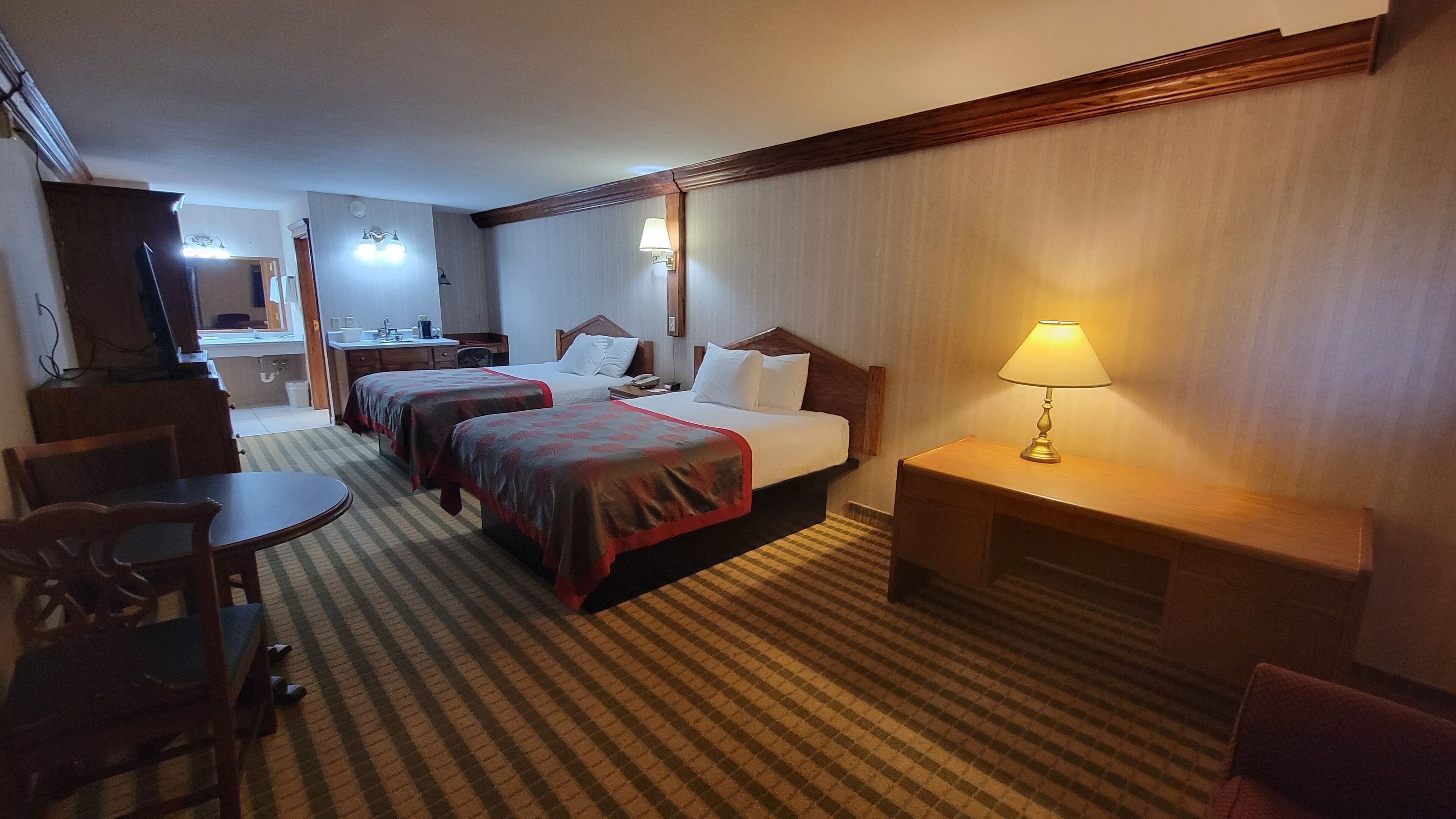 Ett hotellrum med två sängar, ett skrivbord, en stol, en lampa och ett litet bord.