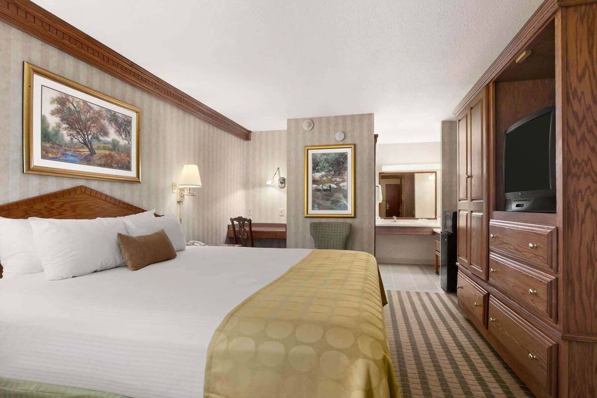 A hotel room with a large bed, a desk with a chair, a television, and a wardrobe.