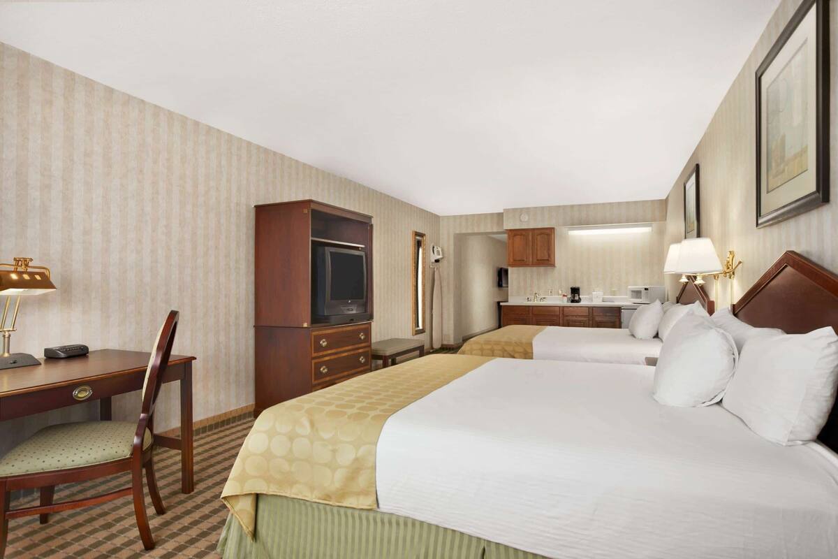 A hotel room with two beds, a desk, a television, a minibar, and a bathroom.
