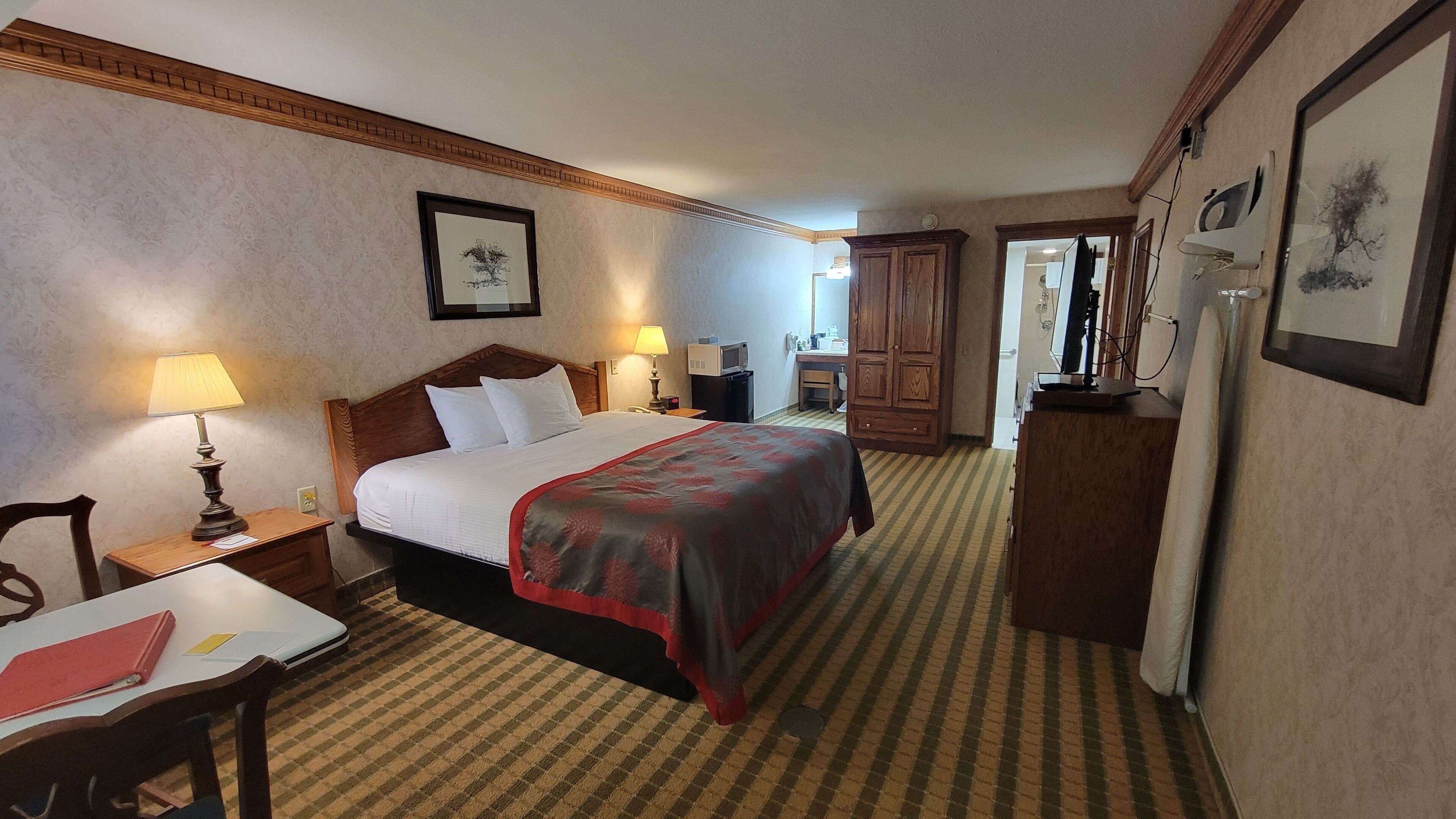 A hotel room with a large bed, a desk, a chair, a dresser, and a mirror.