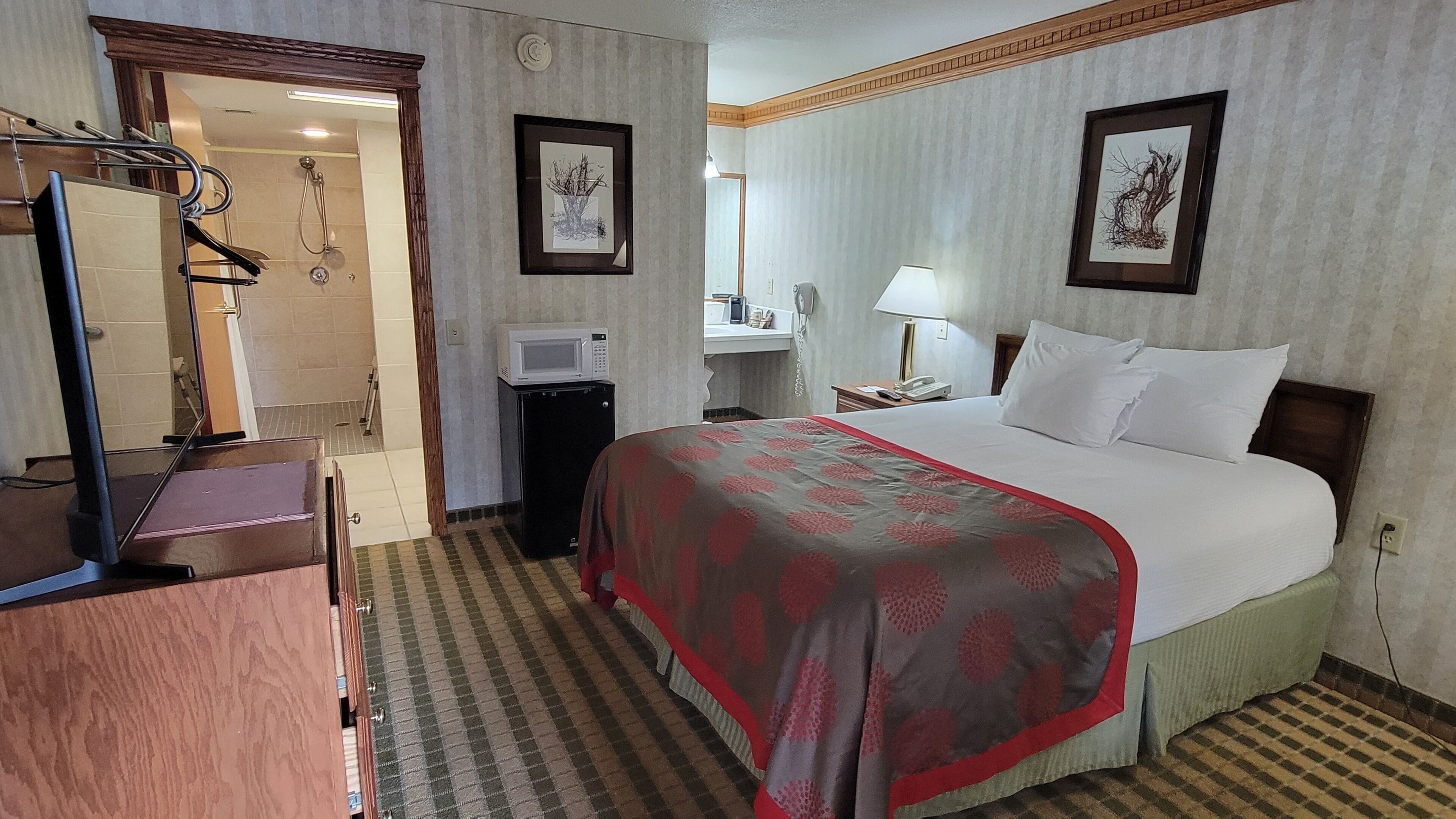 Habitación de hotel con cama, escritorio con computadora, espejo, microondas y teléfono.