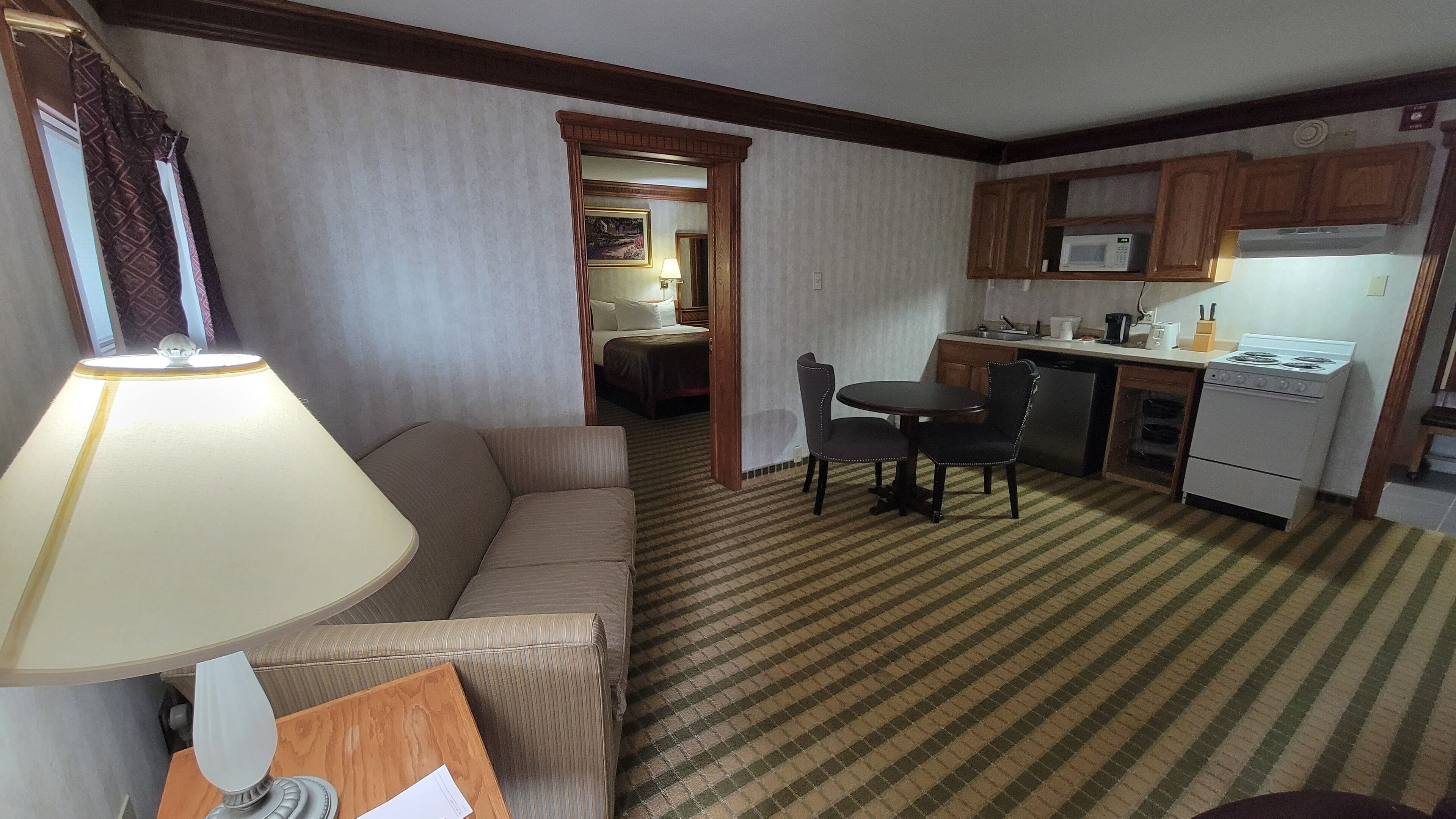 A hotel room with a sofa, a table with chairs, a kitchenette, and a bed in the background.