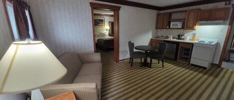 A hotel room with a sofa, a table with chairs, a kitchenette, and a bed in the background.