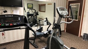 Un espacio de acondicionamiento físico con una máquina elíptica, una cinta de correr y una pantalla de televisión que muestra un programa de ejercicios.