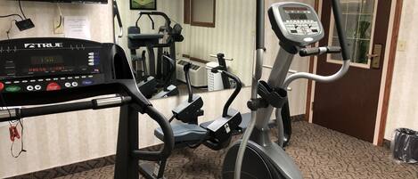 A fitness area with an elliptical machine, a treadmill, and a TV screen displaying a workout program.