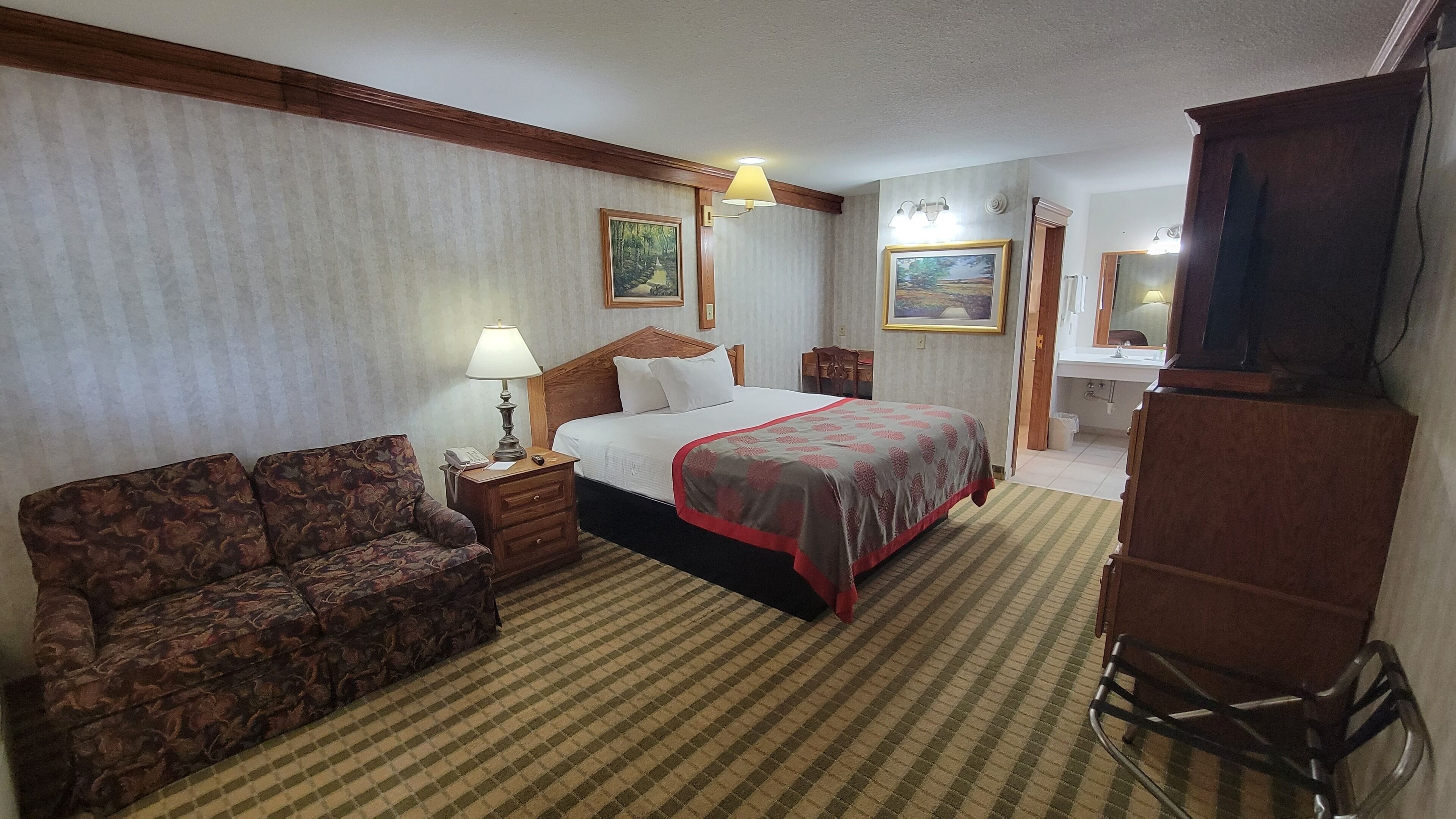 Ein Hotelzimmer mit Bett, Sessel, Schreibtisch, Lampe, Spiegel und Fernseher.