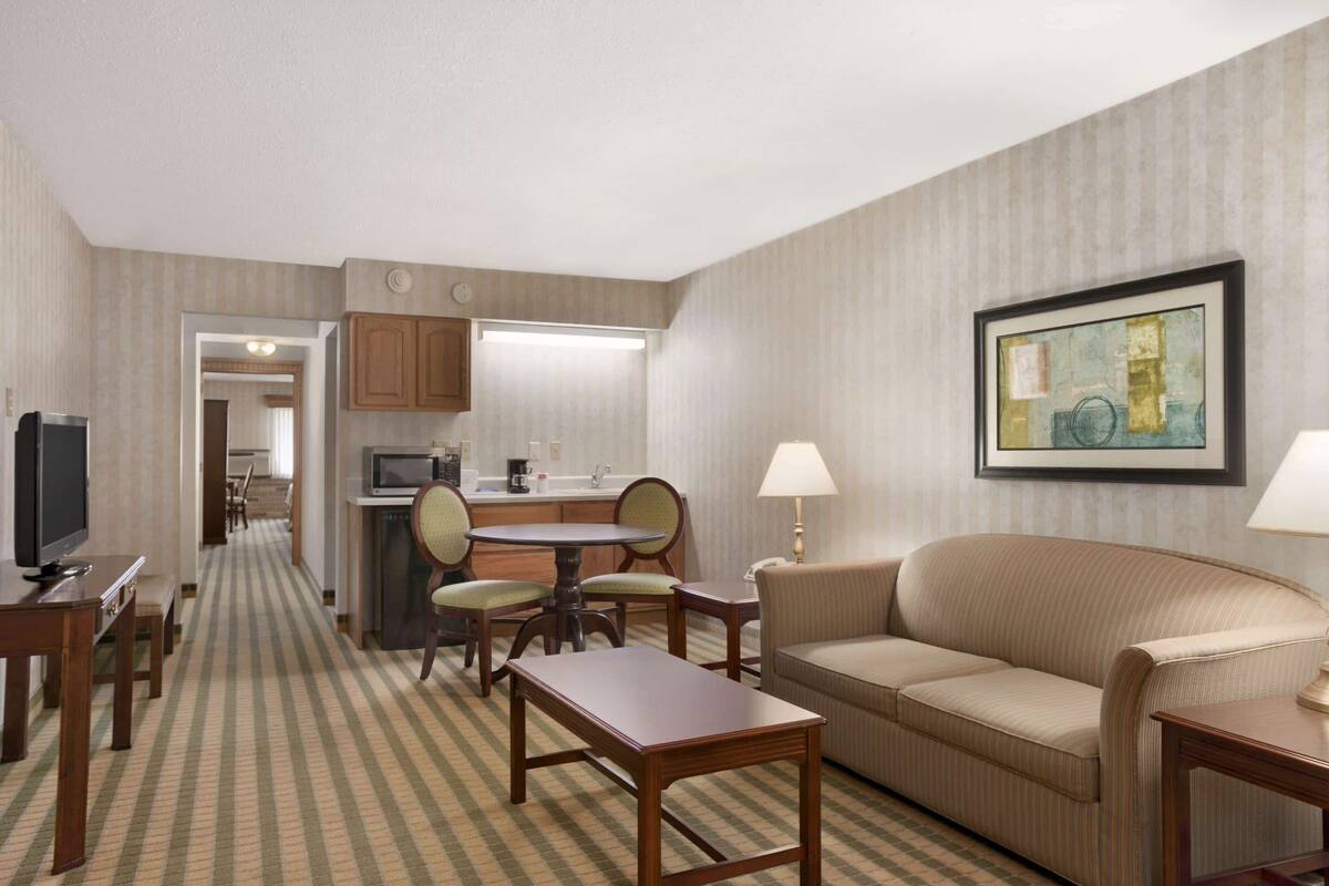 A hotel room with a dining area, a sofa, a TV, and a painting on the wall.