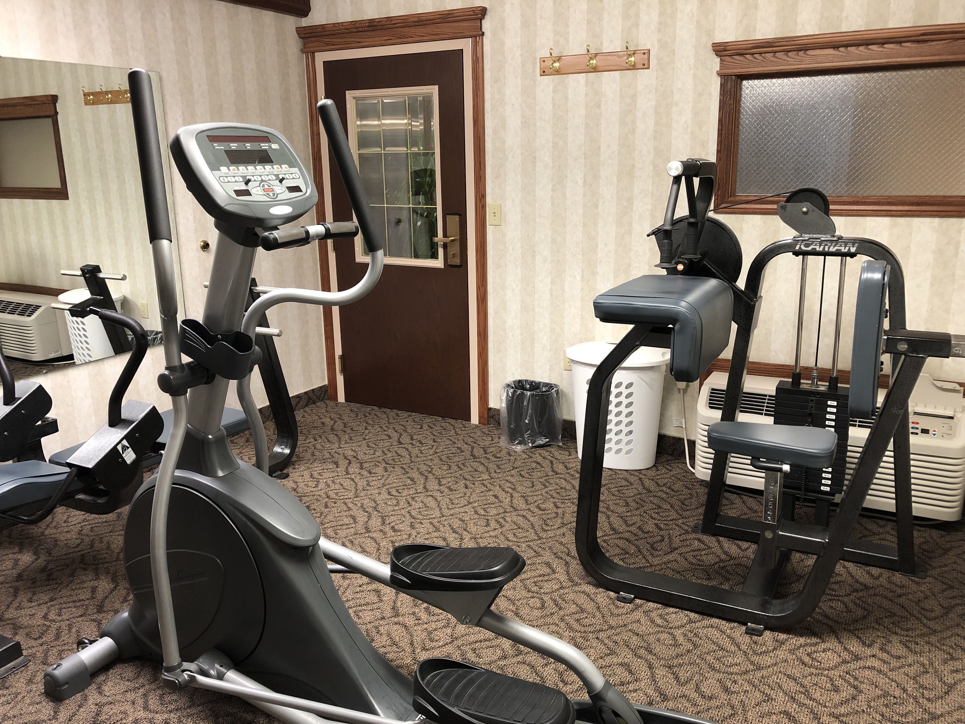 Gimnasio con máquinas de cardio, banco de pesas y espejo.