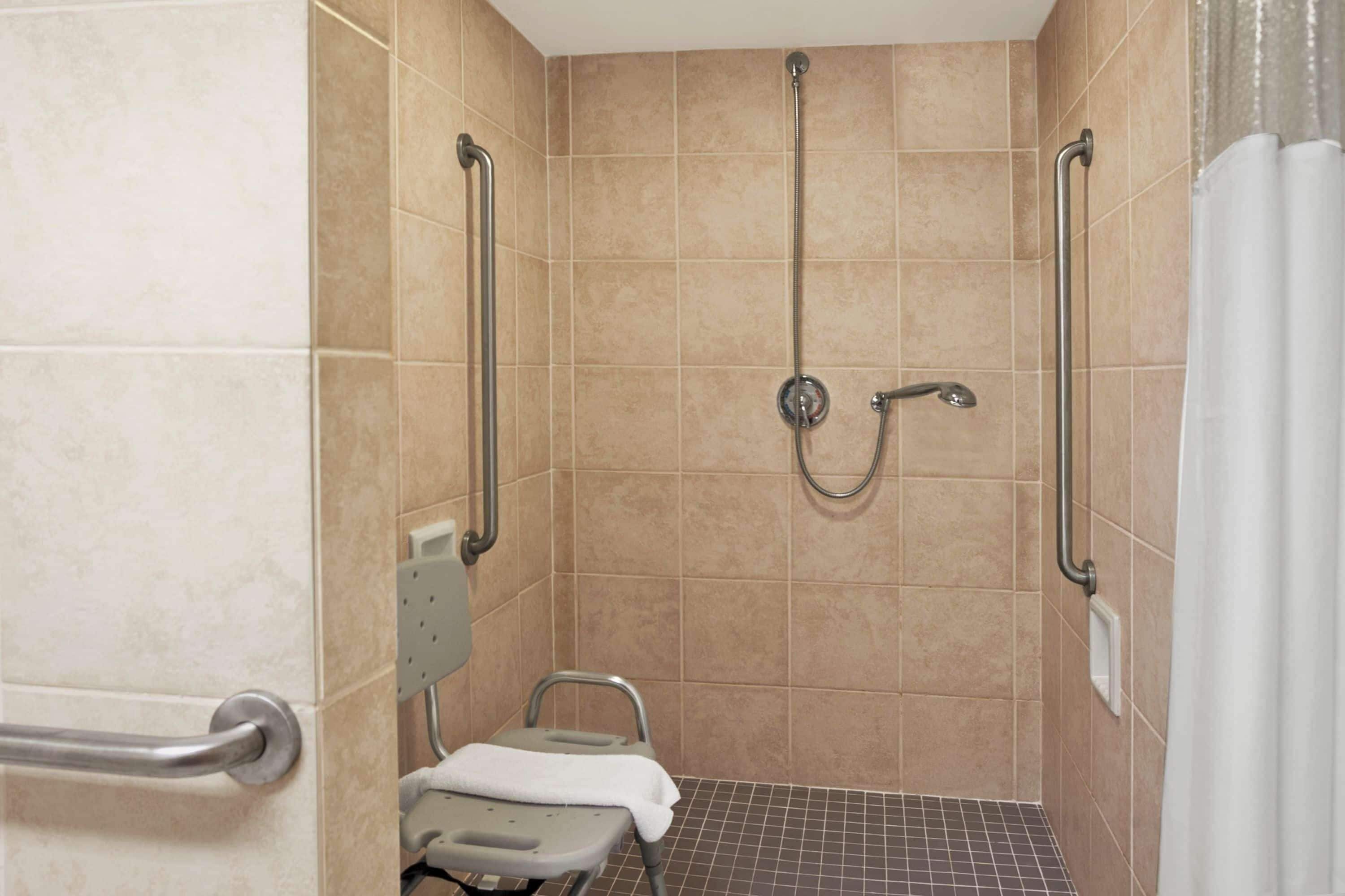 A small, enclosed shower area with a shower chair and grab bars.