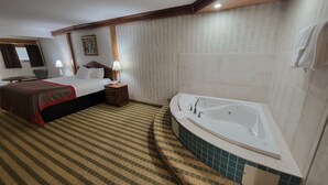 Habitación de hotel con una cama grande, baño independiente con bañera, una mesita con lámpara y un cuadro en la pared.