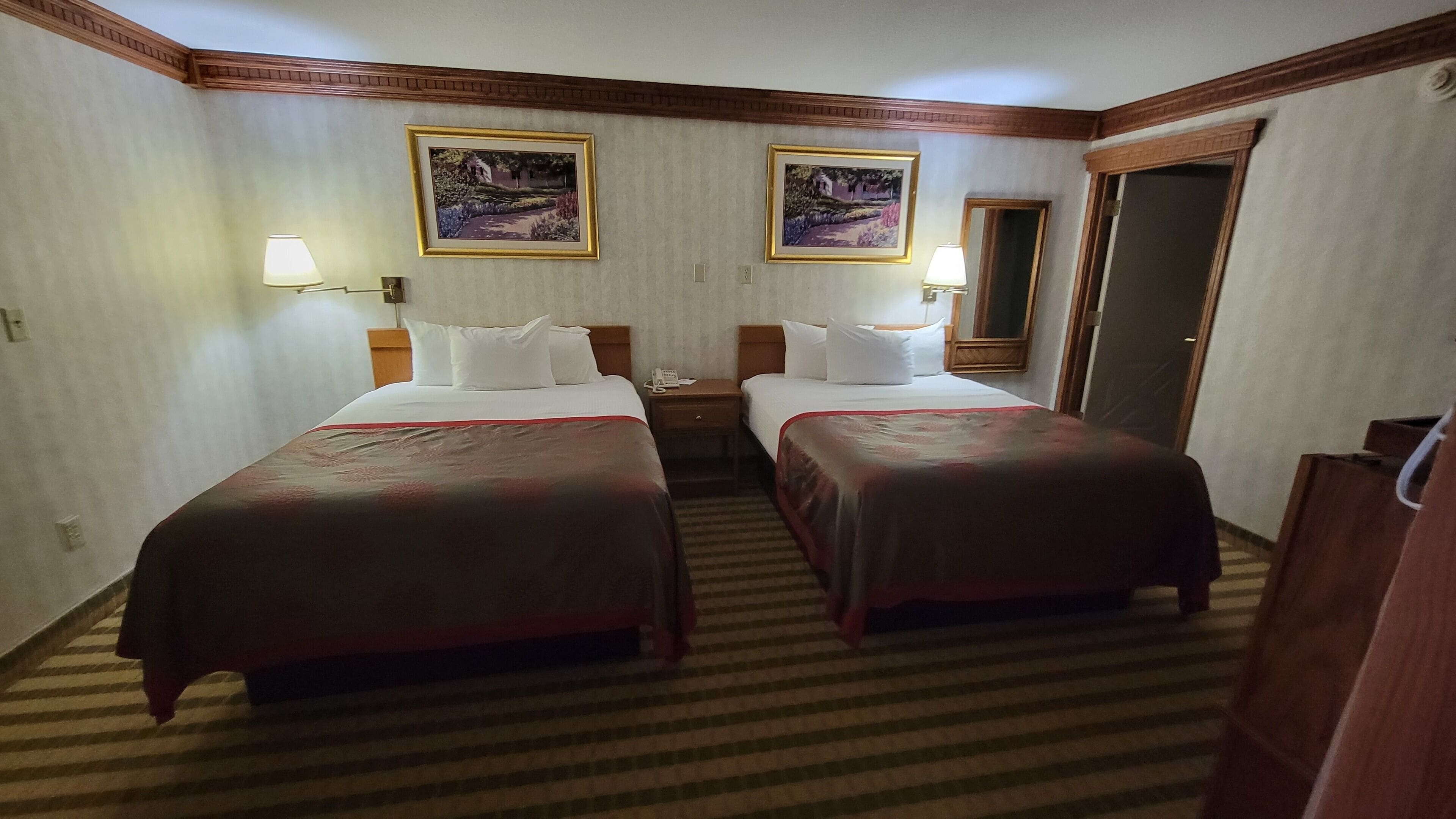 A hotel room with two beds, a nightstand, a telephone, and two framed pictures on the wall.