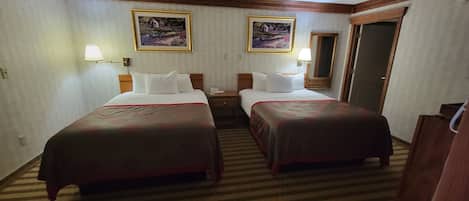 Een hotelkamer met twee bedden, een nachtkastje, een telefoon en twee ingelijste foto’s aan de muur.