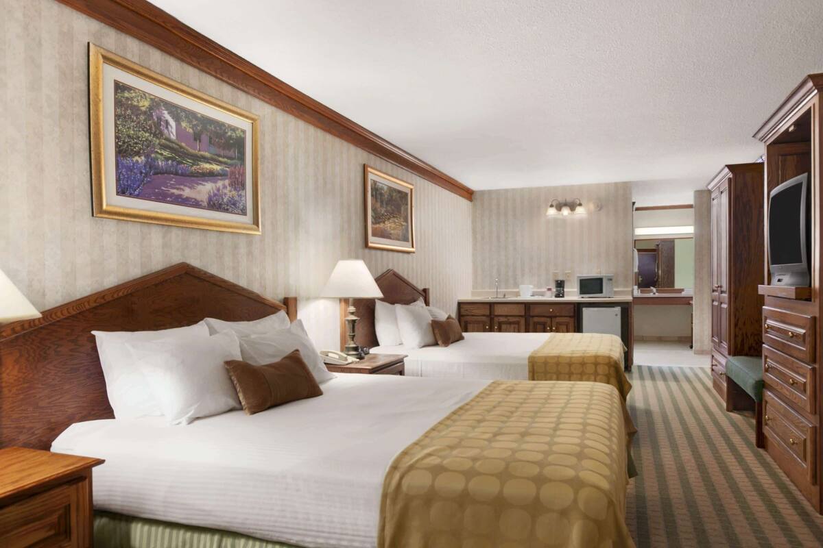 A hotel room with two beds, a desk, a microwave, and a television.