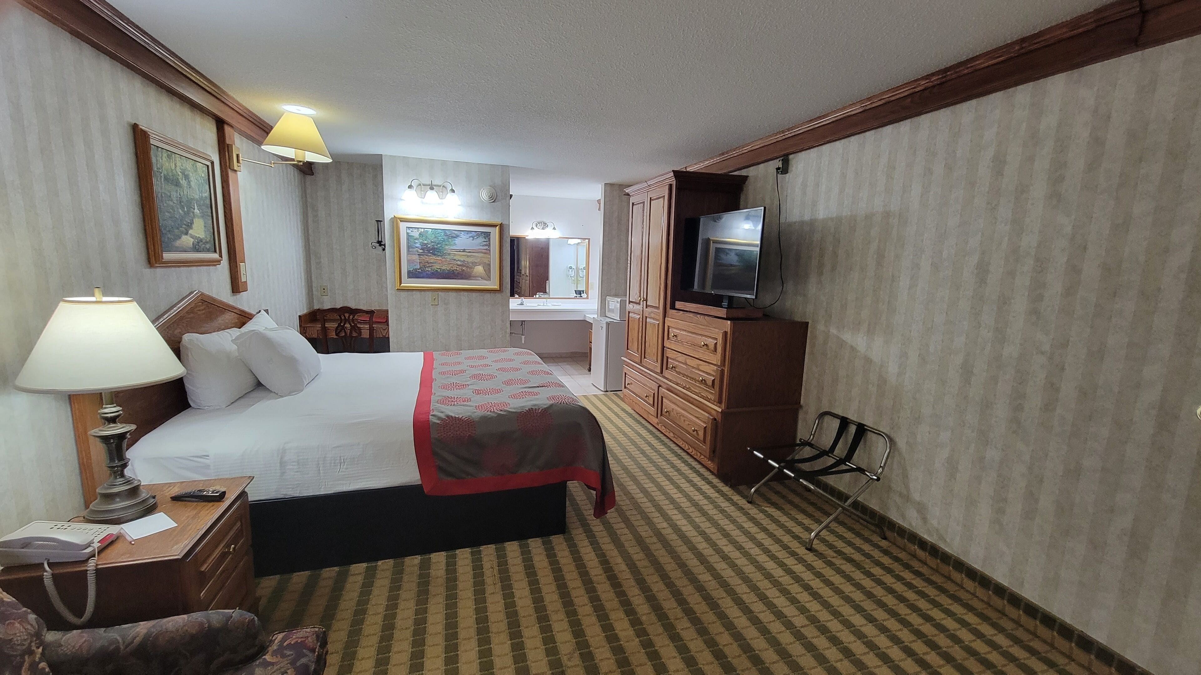 A hotel room with a bed, a desk, a chair, a television, and a bathroom.