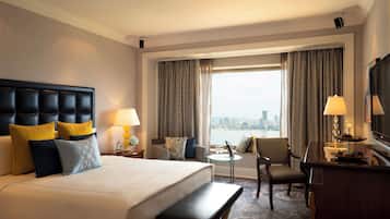 A hotel room with a large bed, a desk, a chair, and a view of the city through the window.