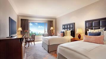 A hotel room with two beds, a desk, a TV, and a view of the sky.