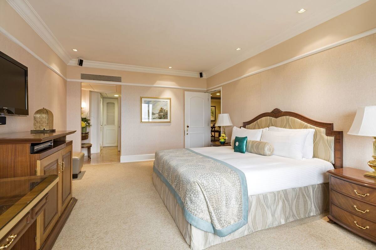 A bedroom with a bed, a dresser, a television, and a door leading to another room.