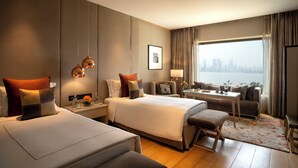 A hotel room with two beds, a sofa, a dining table, and a view of the city.