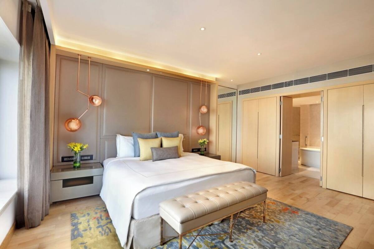 A modern bedroom with a large bed, bedside tables, a bench, and a walk-in closet.